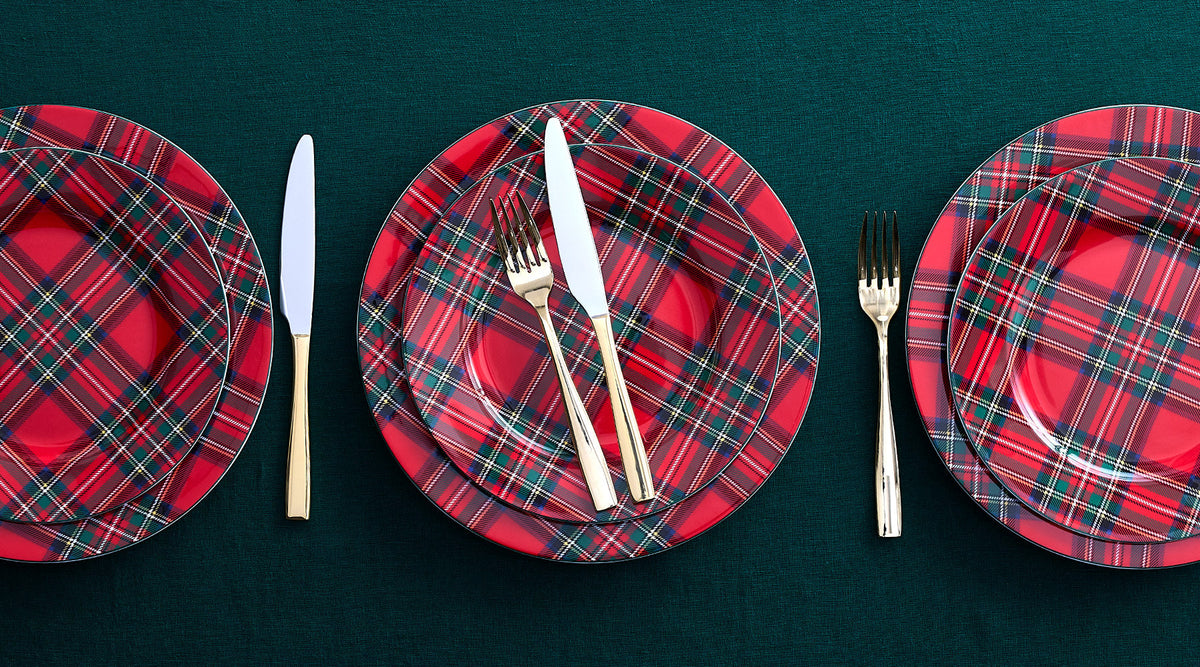 Three red tartan dinner plates on a dark green table with gold cutlery arranged around the center plate