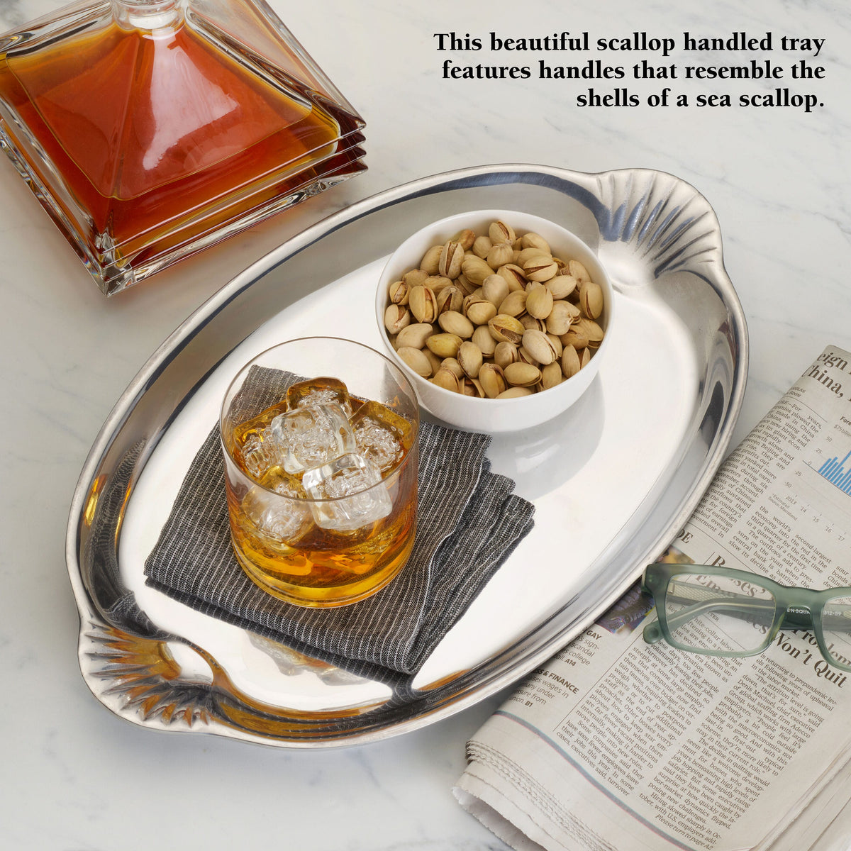 Scalloped handle oval glass tray with an amber bottle and a bowl of pistachios on it