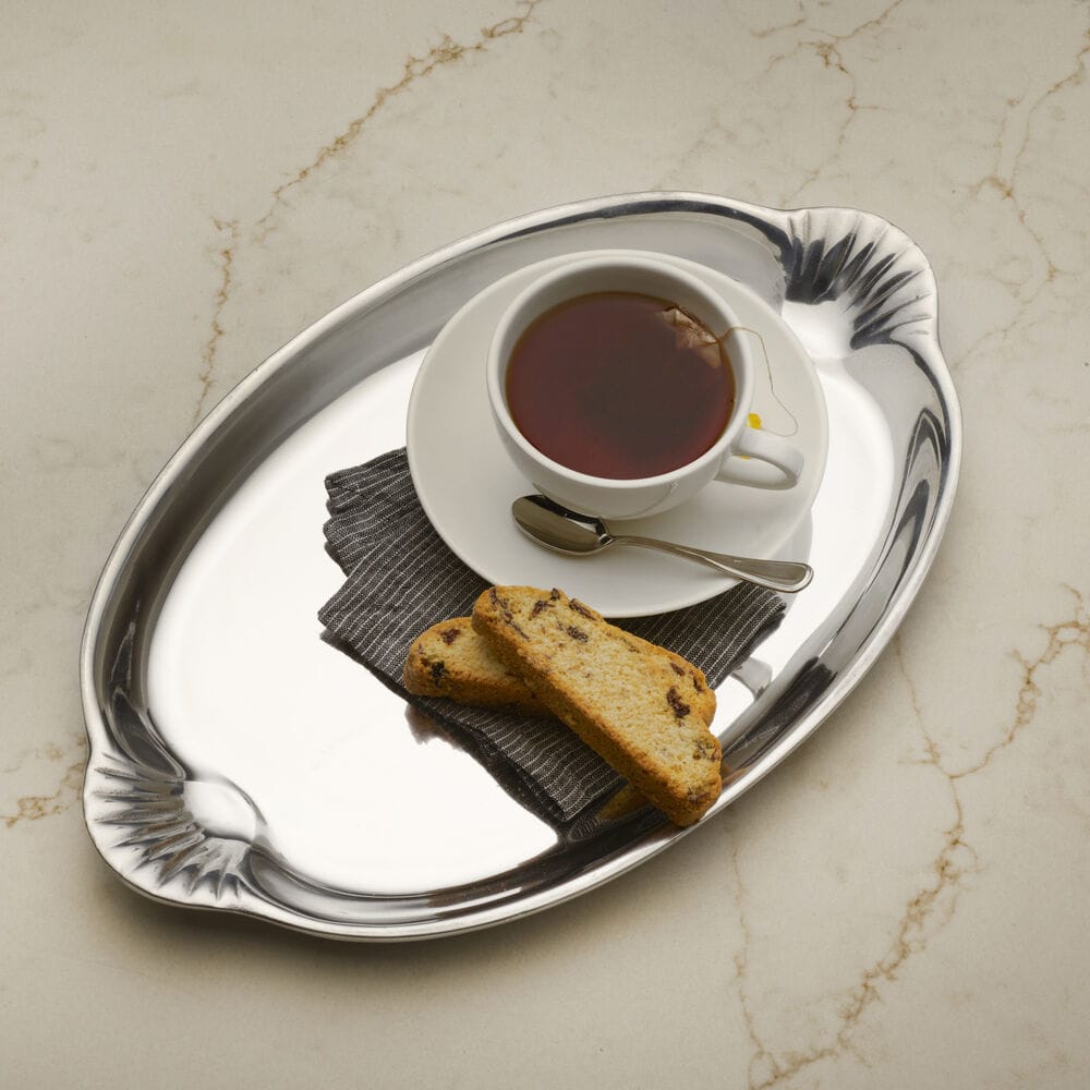 Scallop handle oval silver serving tray with teacup on a saucer and two biscotti on a striped napkin