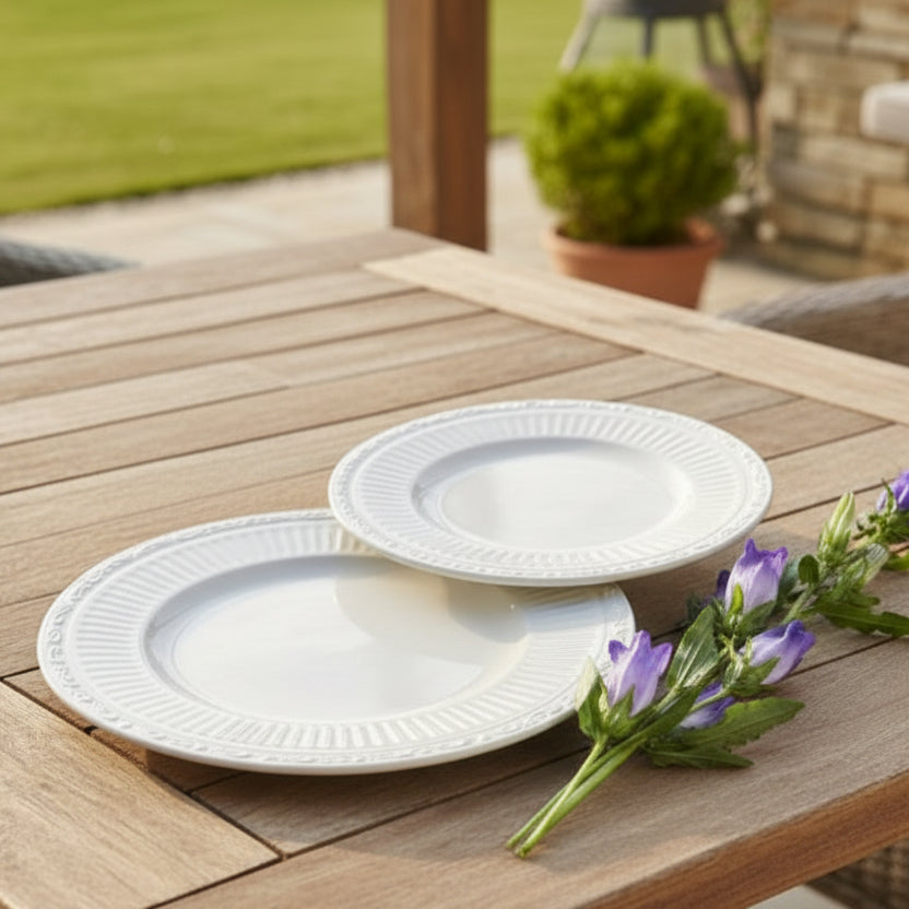 White melamine plates on a wooden table with purple flowers, outdoor setting.