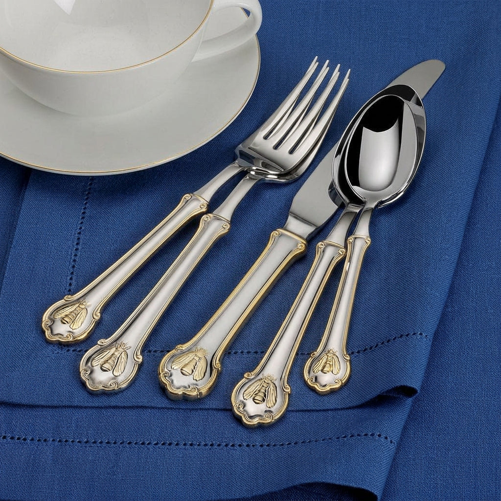 Napoleon Bee gold accented flatware arranged on a napkin beside a teacup and saucer.